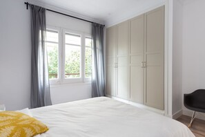 A bedroom with a bed, grey curtains, a window, and a wardrobe. - Casa Cosi - Eixample 2 (Barcelona)