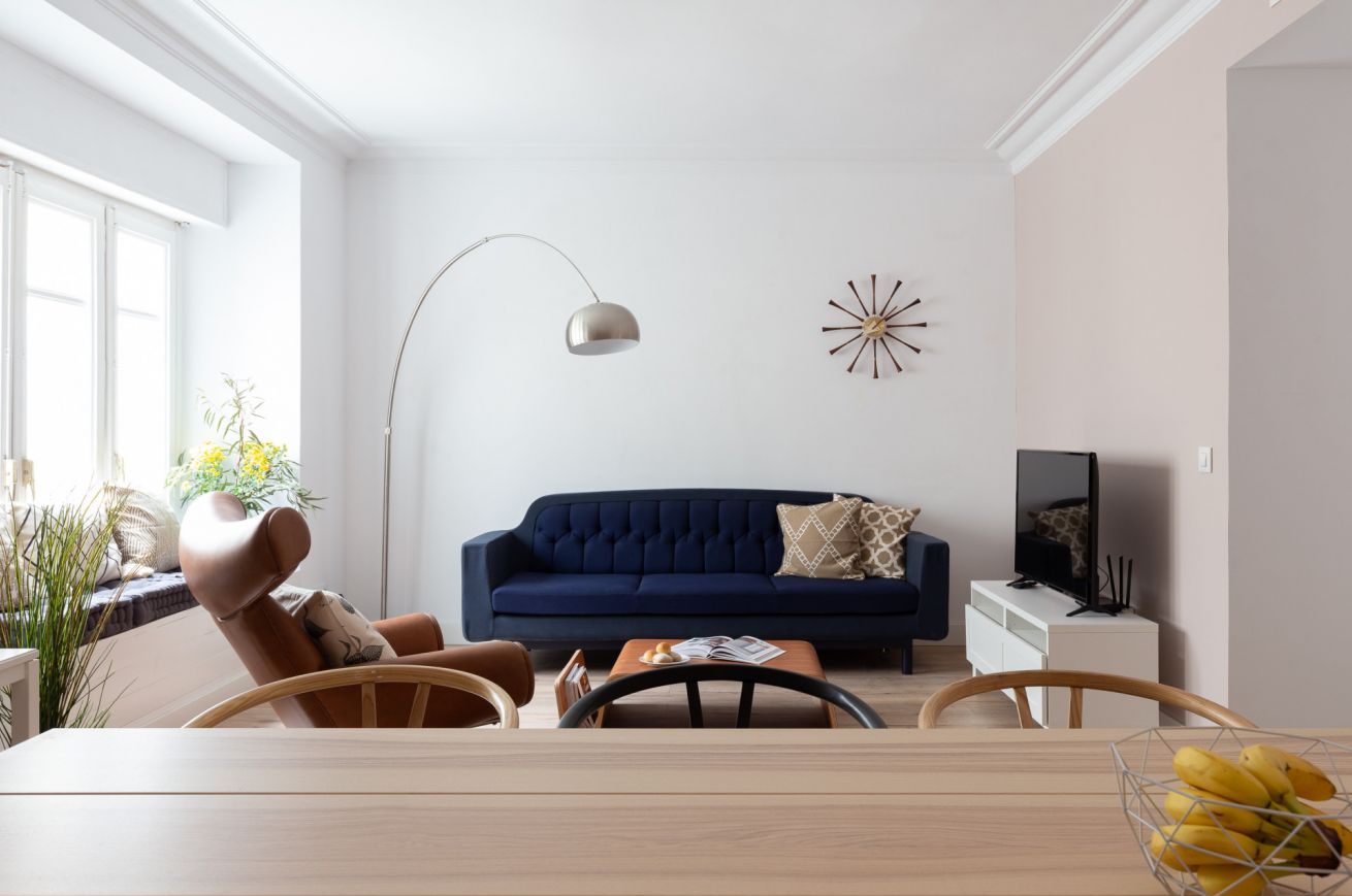 A modern living room with a dark blue sofa, a wooden dining table, and a floor lamp.