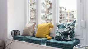 Asiento junto a la ventana con cojines azul turquesa, un cojín amarillo y un cojín estampado.