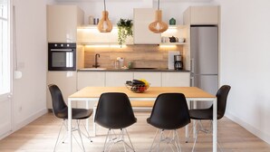 Una cocina moderna con una mesa de madera, cuatro sillas negras, un refrigerador y lámparas colgantes.