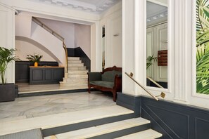 Una imponente escalera con acabado de madera oscura y barandilla de latón, que conduce a un rellano con un banco de madera oscura y una planta en maceta.