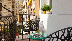 A balcony with a glass table, two chairs, a potted plant, and a magazine.