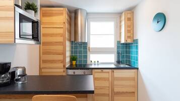 Een kleine keuken met houten kastjes, een zwart aanrecht, een rvs afzuigkap en een klok aan de muur.