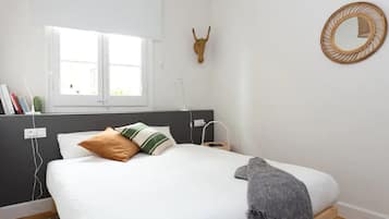 Een slaapkamer met een bed, een raam, een spiegel aan de muur en een decoratief object.