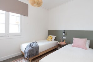 A bedroom with two beds, a small bedside table, a lamp, and a window.
