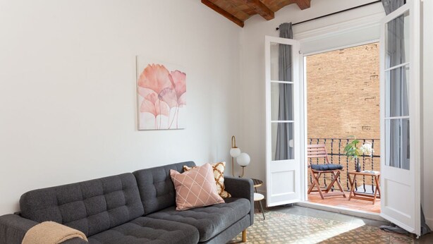 Un salon moderne avec un canapé gris foncé, un tapis à motifs et une grande fenêtre donnant sur un balcon.