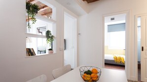 Une pièce moderne et bien éclairée, avec une table à manger, un panier de fruits et un lit en arrière-plan.
