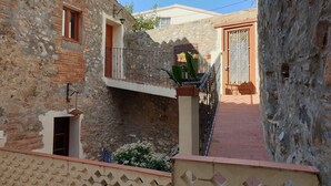 A narrow courtyard with stone walls, a small balcony with a metal railing, and a potted plant. - Family apartment located between the Priorat wine district and the beach in Cambrils (Duesaigües)