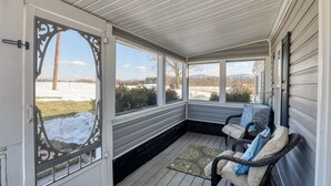 A covered porch with a view of a snowy landscape, two wicker chairs, and a patterned rug. - Country cottage beside stocked pond on 40 acres and Blue ridge Mountain View (Front Royal)
