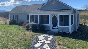 A single-story house with a porch, a stone pathway leading to the entrance, and a clear sky. - Country cottage beside stocked pond on 40 acres and Blue ridge Mountain View (Front Royal)
