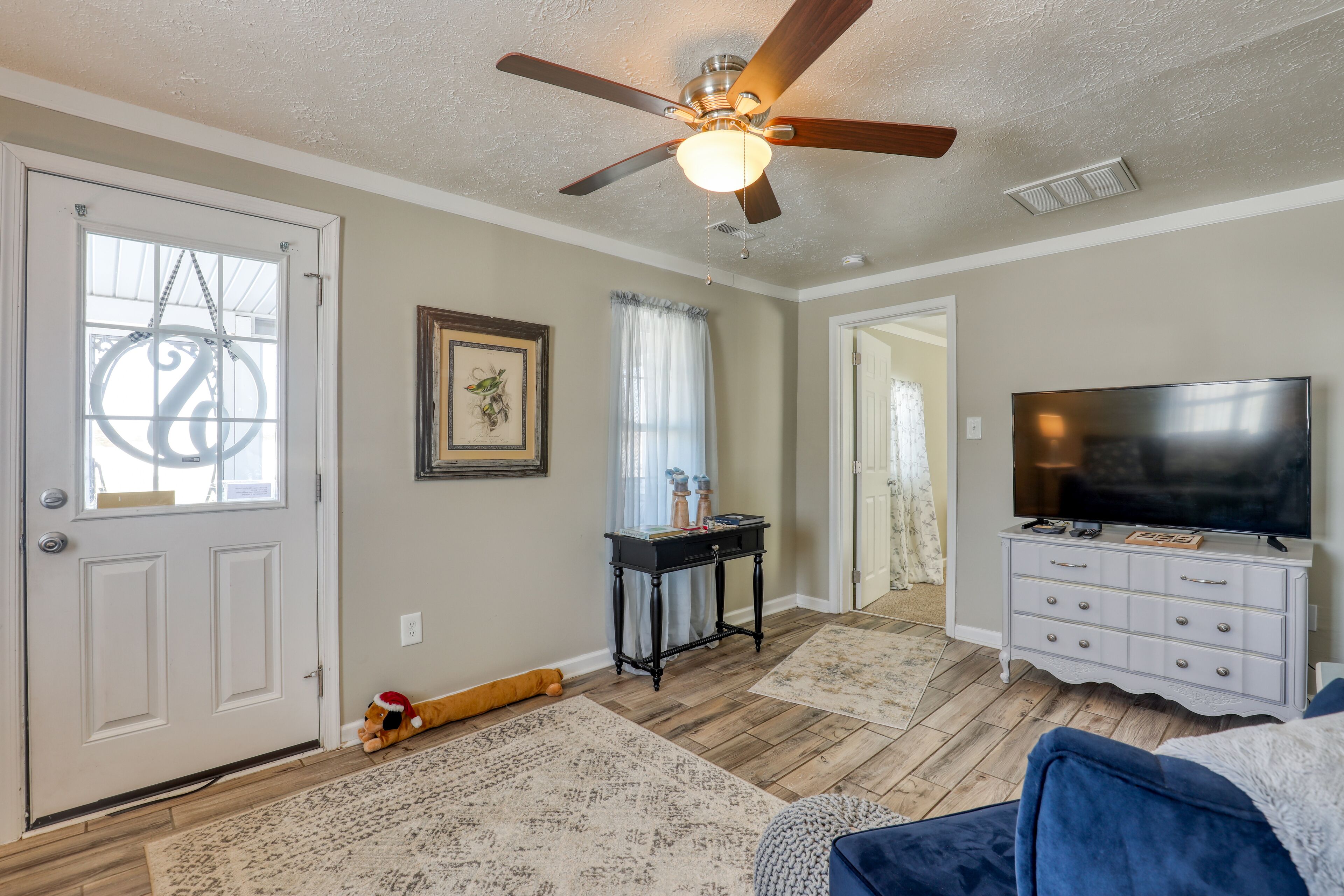 A living room with a ceiling fan, a TV on a white dresser, a door with a decorative glass panel, and a rug on the floor.