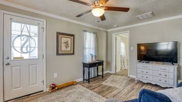 A living room with a ceiling fan, a TV on a white dresser, a door with a decorative glass panel, and a rug on the floor.