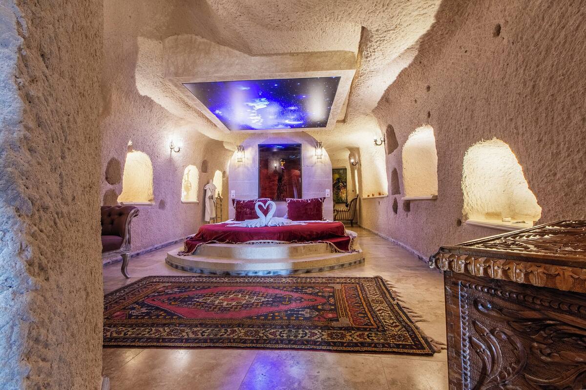 A luxurious room with a central bed, a ceiling projection, and stone walls.
