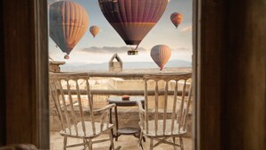 Un balcon avec des fauteuils en osier et une petite table, offrant une vue sur les montgolfières.