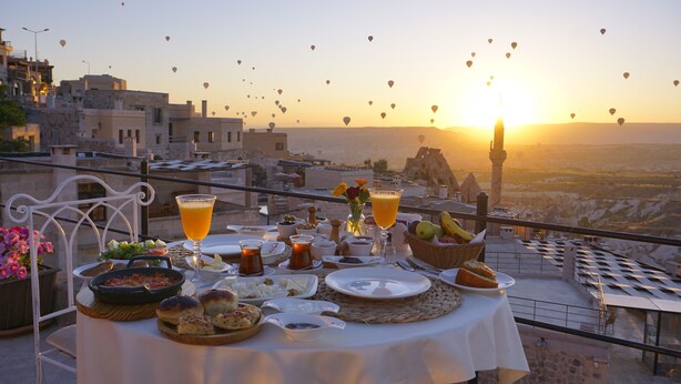 Une table dressée avec une variété de plats et de boissons, et une vue sur des montgolfières au coucher du soleil.