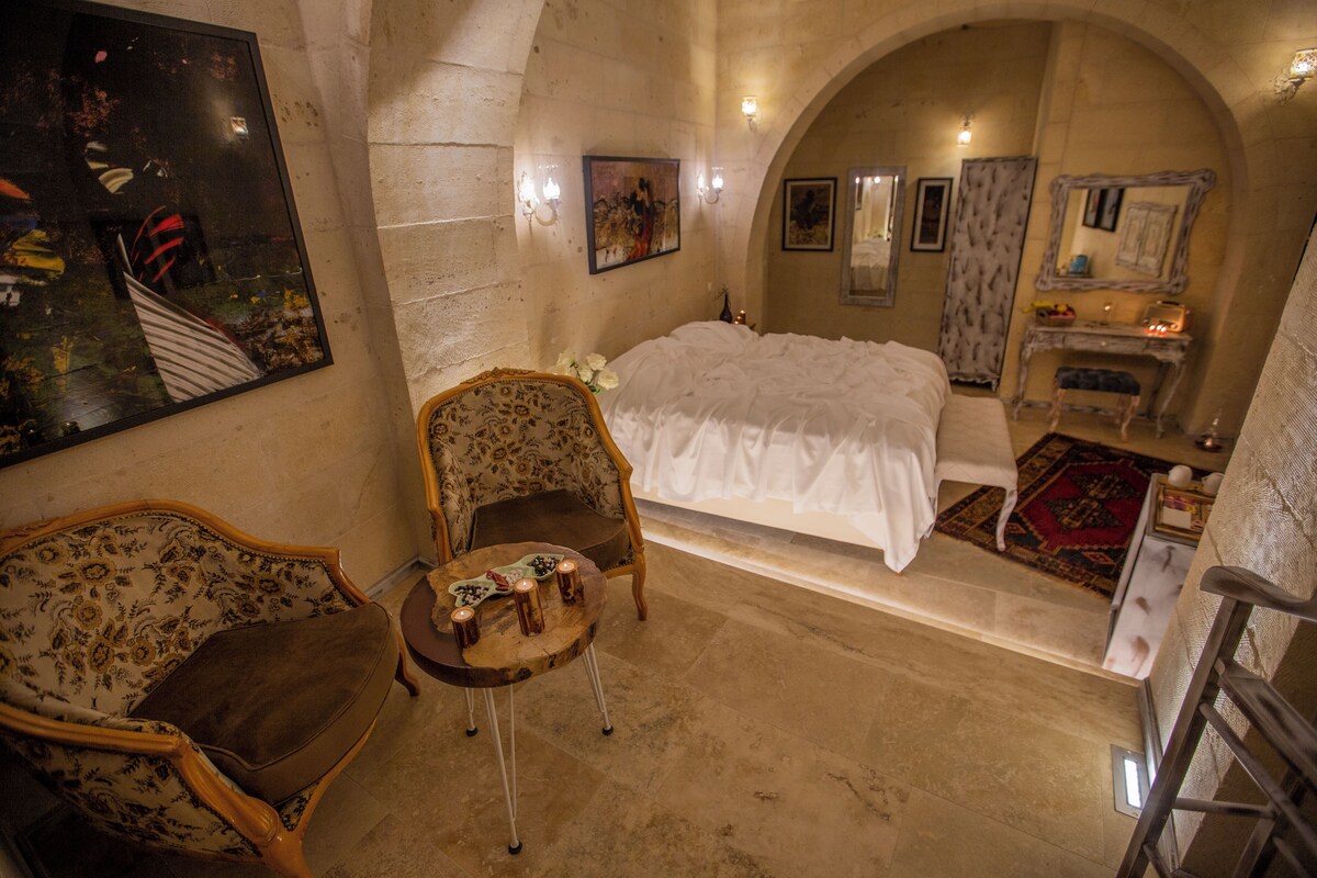 A bedroom with a bed, a chair, a small table with candles, and a painting on the wall.