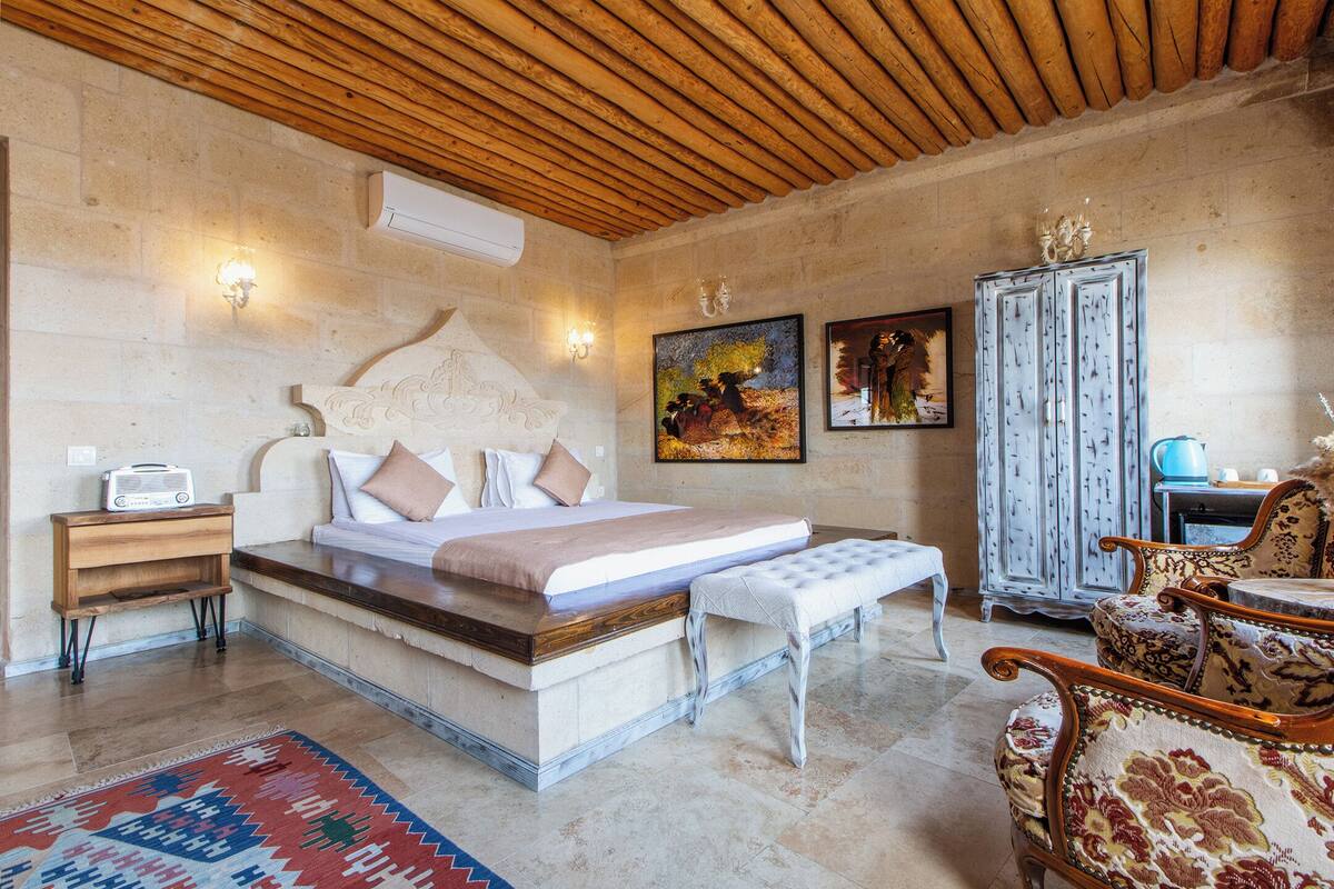 A bedroom with a wooden ceiling, a bed with a headboard, a nightstand, a bench, a cabinet, and a chair.