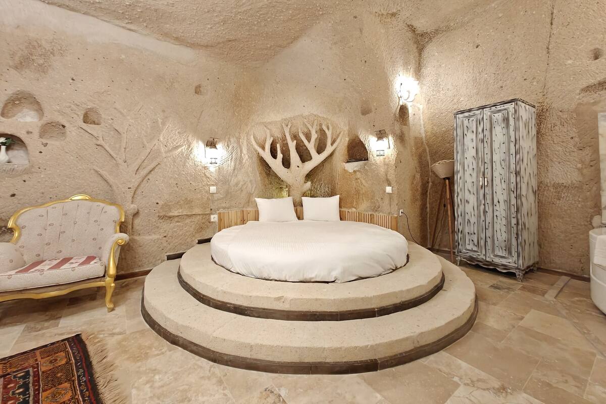 A room with a central bed, a round seating area, a decorative tree wall, and a wardrobe.