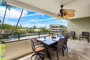 A balcony with a table set for two, chairs, and a ceiling fan. - White Sands Village #226 Updated, OceanViews, Elevators, Central AC! (Kailua-Kona)