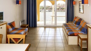 Habitación de hotel con cama, dos sillas, una mesa, televisor y balcón con cortinas.