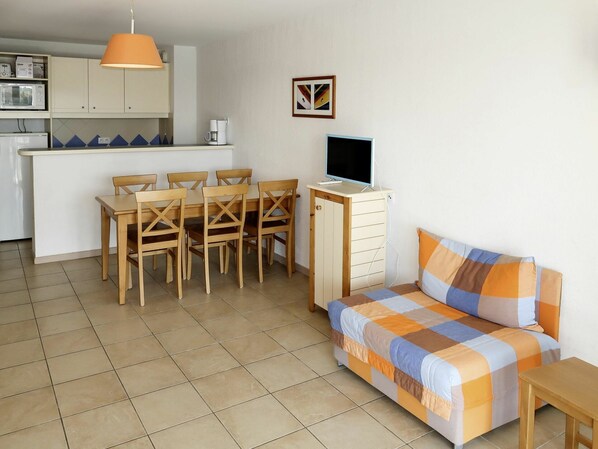 Un espacio habitable compacto con zona de comedor, kitchenette y cama con manta a cuadros.