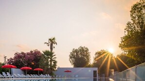 A swimming pool with clear water, surrounded by lounge chairs and umbrellas, reflecting the sunset. - Nice apartment in villa for 6 people with WIFI, A/C, pool, TV, terrace and pets allowed (Argelers)