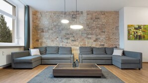 Una sala de estar moderna con una pared de piedra, dos sofás grises, una mesa de centro de madera y un ventanal grande.
