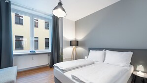 Una habitación de hotel moderna con una cama grande, una mesita de noche con lámpara, una ventana con cortinas y vistas del edificio exterior.
