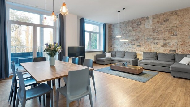 Una sala de estar moderna con una mesa de comedor de madera, sofás grises y una pared de ladrillo.