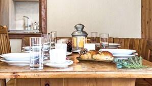Une table de salle à manger en bois, mise avec des assiettes, des verres, une bougie, une lanterne et du pain.