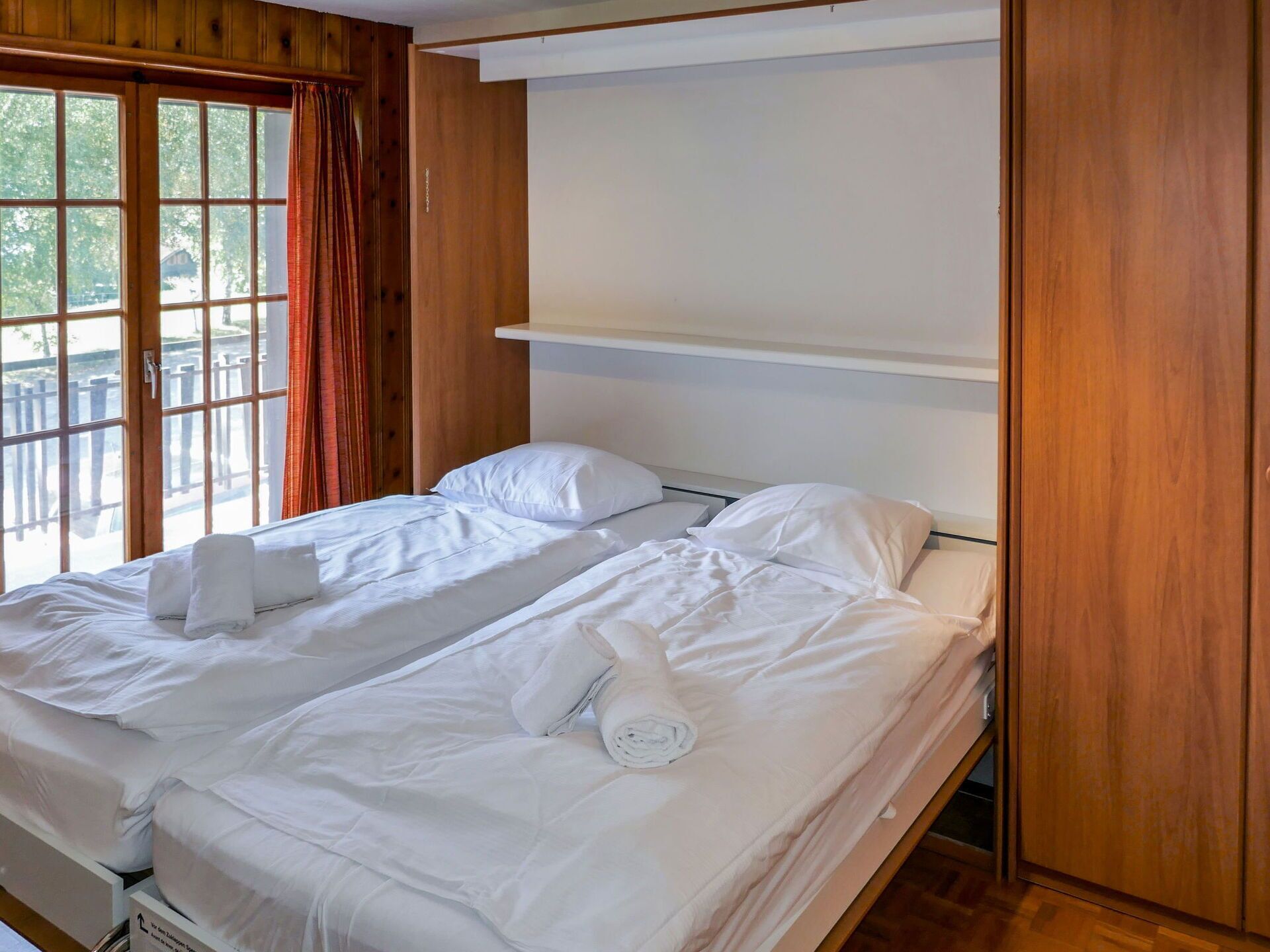 Ein Doppelbett mit weißen Leinen und Kissen, ein Holz-Kopfteil und ein Fenster mit Vorhängen.