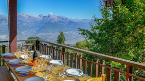 Une table à manger dressée avec des assiettes, des couverts et des verres, donnant sur un paysage montagneux.