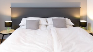 Una cama bien tendida con ropa blanca, dos mesitas de noche con lámparas y un cabecero moderno.