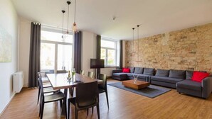 A modern living room with a dining area, a stone wall, and a large window.