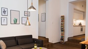 A modern living room with a sofa, a coffee table, and a stack of books against the wall.