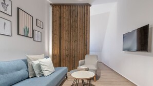 Ett modernt vardagsrum med en blå soffa, ett runt soffbord, en vit fåtölj och en vägg av trä. En platt-TV är monterad på väggen.