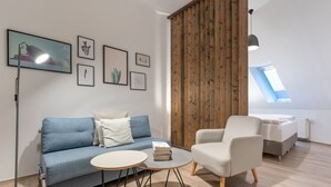 Ett modernt vardagsrum med en blå soffa, en vit fåtölj, ett runt soffbord och en avskärmande väggpanel i trä.