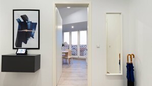 En hall med en inramad abstrakt målning, ett litet skrivbord med en surfplatta, en dörr och ett par paraplyer.