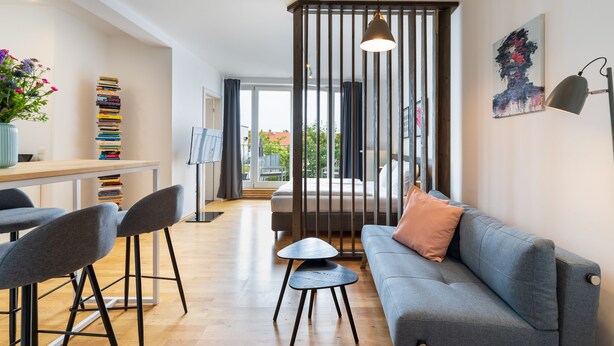A modern living room with a grey sofa, a small table, and a tall stack of books on a shelf.