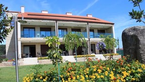 A two-story building with a red-tiled roof, multiple balconies, and a well-maintained garden with yellow flowers.