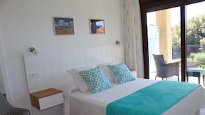 A bedroom with a bed, a nightstand, a chair, and a view of the outdoors through a glass door.