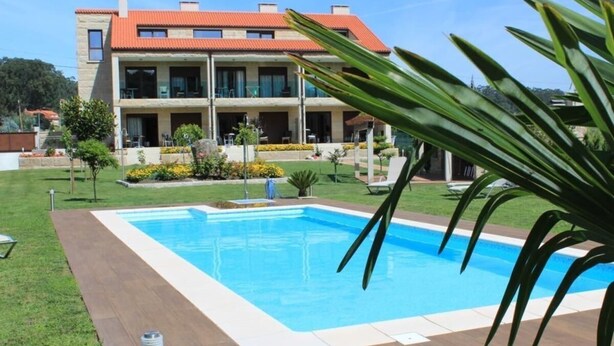 A modern two-story building with a swimming pool, surrounded by well-maintained lawns and tropical plants.