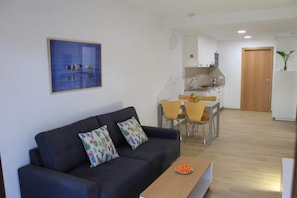 A living room with a sofa, a dining table with chairs, a kitchen area, and a door.