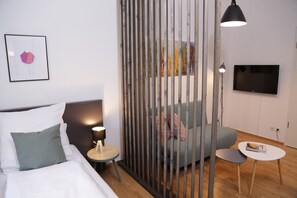 Una habitación de hotel moderna con cama, sofá, una mesita, televisor y un separador decorativo.