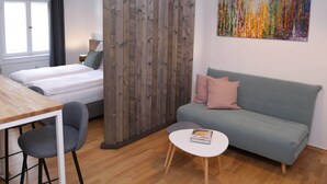 Une pièce comprenant un lit, un canapé, une table à manger avec des chaises, une petite table blanche avec un livre, une suspension noire et une peinture abstraite colorée accrochée au mur.