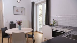 A modern kitchen with white cabinets, a black countertop, and a built-in oven. There is a dining area with a round table and chairs, and a vase with flowers on the table.