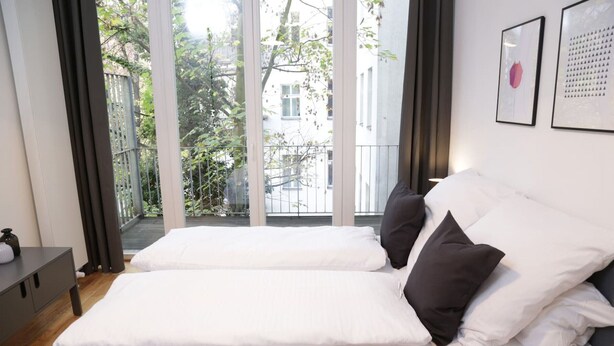 A hotel room with a bed, a bedside table, and a view through a large window.