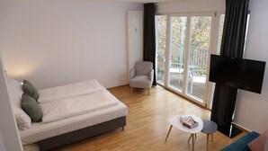 Une chambre d’hôtel moderne, équipée d’un lit, d’une chaise, d’une petite table, d’un téléviseur et d’un balcon avec une rambarde.