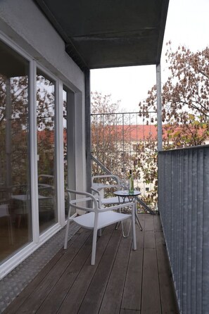 Enjoy the serene view from this balcony with a glass door leading to the indoor space, featuring a comfortable seating area with two chairs and a small table.
