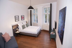 A bedroom with a bed, a bedside table, a lamp, a sofa, and a painting on the wall. - Bright and modern 2-room apartment in Prenzlauer Berg (3) (Berlin)